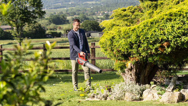 Homme tenant et utilisant un souffleur à batterie dans un jardin