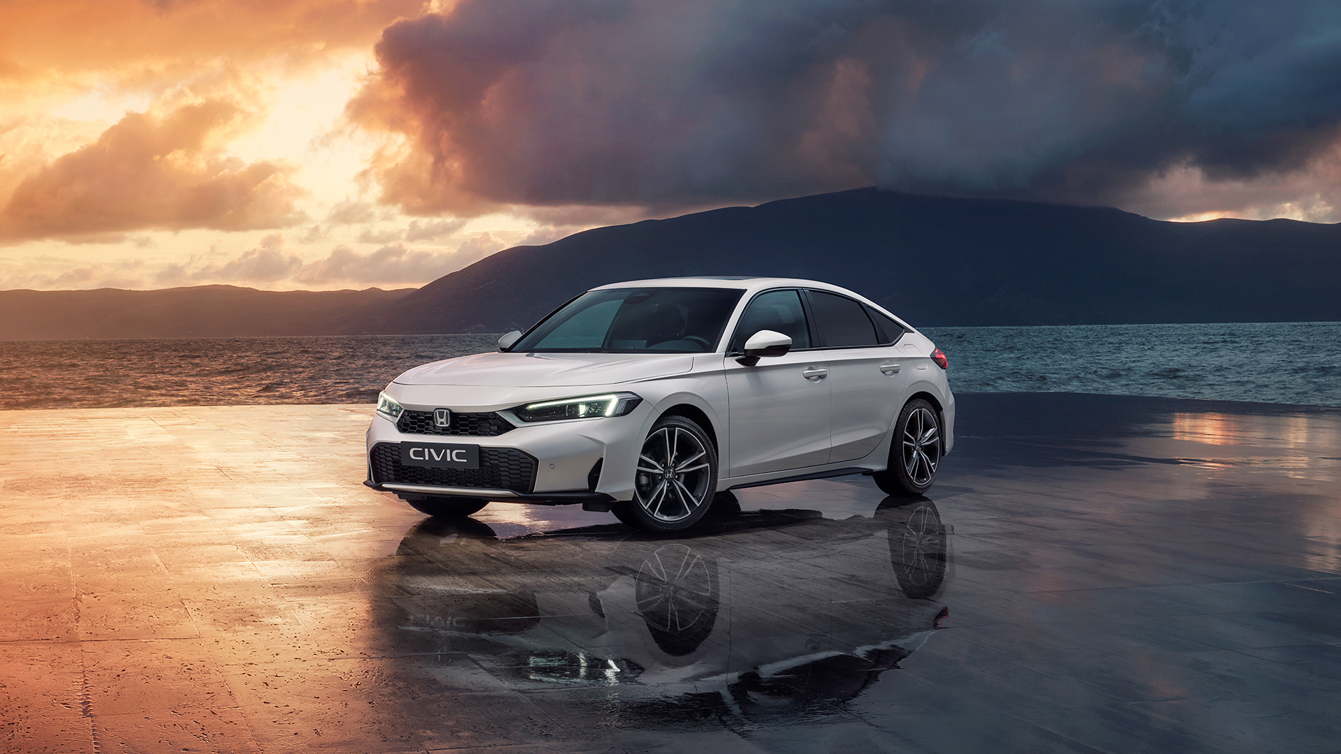 Civic Hybrid garée à côté d'un océan au coucher du soleil.