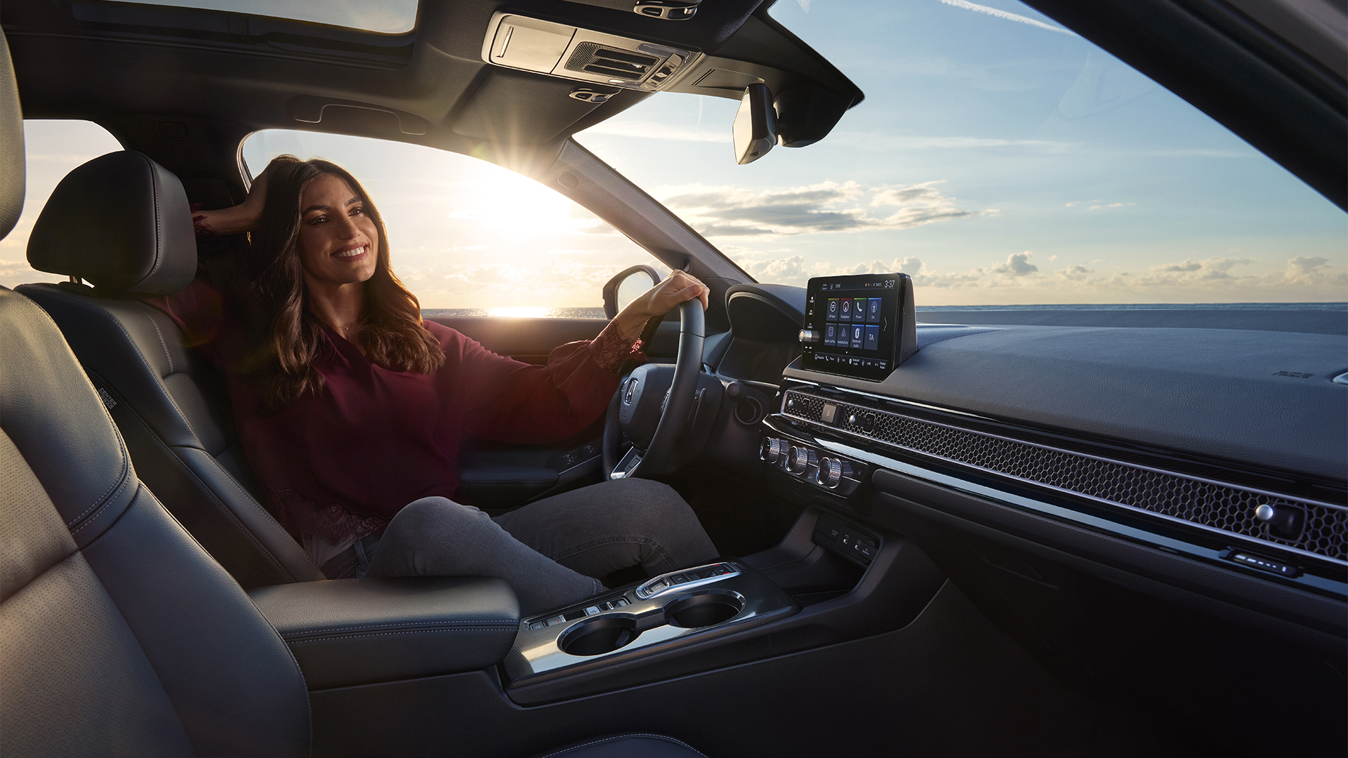 Photo prise depuis l'intérieur de la Civic Hybrid, une femme assise dans la voiture, au bord de la mer.
