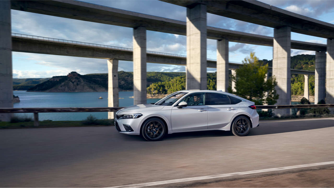 Vue latérale de la Honda Civic e:HEV garée face à la mer. 