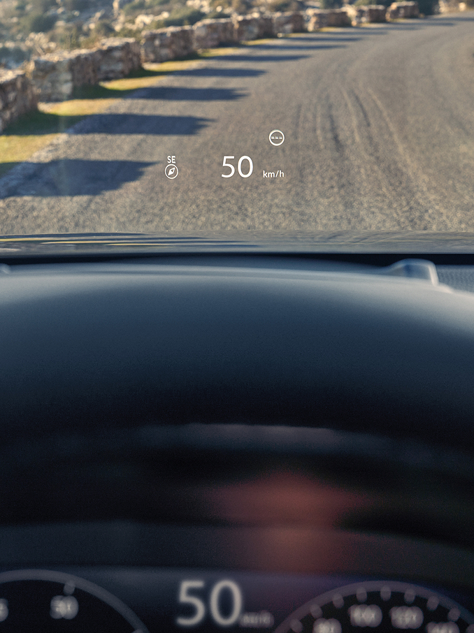 Une vue à la première personne depuis le siège du conducteur montrant un affichage tête haute (HUD) projetant « 50 km/h » et une boussole sur le pare-brise au-dessus d'une route en gravier.