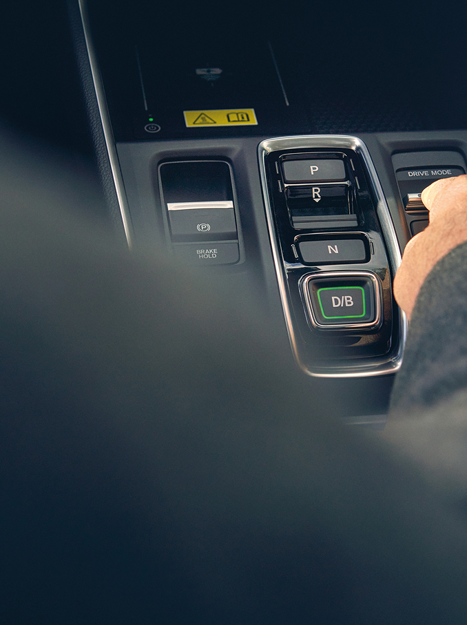 Une main s'approche d'un interrupteur à bascule sur la console centrale d'une voiture moderne, à côté des boutons de sélection des vitesses.