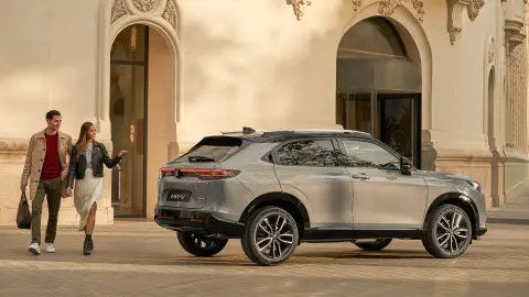 Vue latérale du Honda HR-V à l'extérieur d'un hôtel, avec un couple qui passe. 