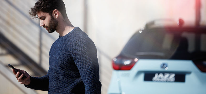 Man looking at My Honda Plus App with Honda Jazz Hybrid Crosstar behind. 