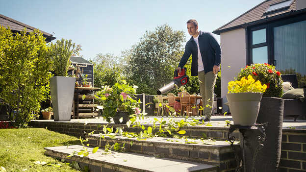 Homme tenant et utilisant un souffleur à batterie sur le patio