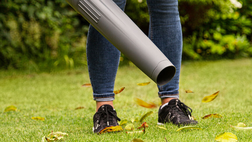 Femme en baskets utilisant un souffleur de feuilles à batterie