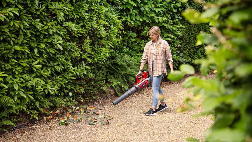 Femme en baskets utilisant un souffleur de feuilles à batterie