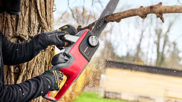 Une tronçonneuse à batterie HONDA coupant une branche d'arbre.