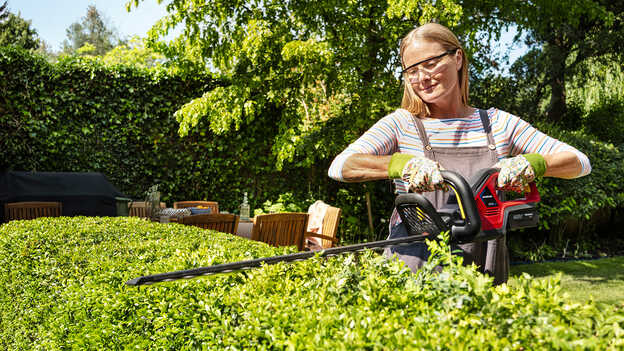 Femme taillant une haie avec un taille-haie à batterie Honda dans un jardin.