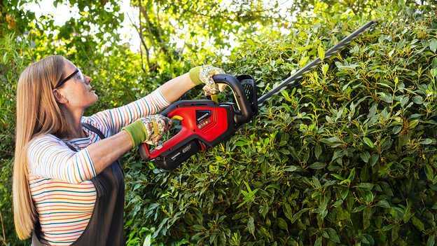 Femme taillant des buissons avec un taille-haie à batterie Honda dans un jardin.