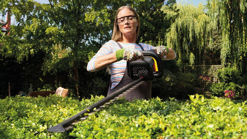 Femme utilisant un taille-haie à batterie Honda pour tailler une haie dans un jardin.