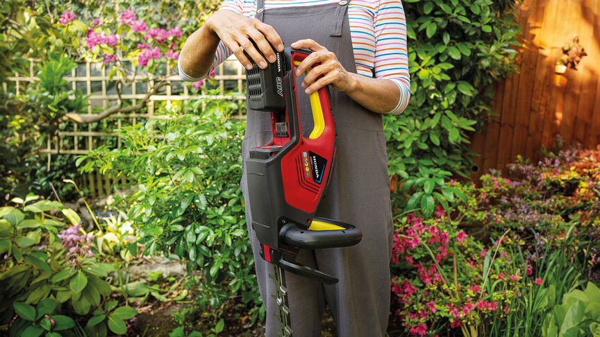 Femme utilisant un taille-haie à batterie Honda pour tailler une haie dans un jardin.