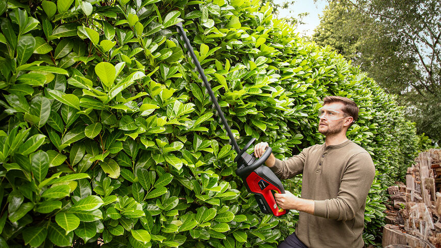 Femme utilisant un taille-haie à batterie Honda pour tailler une haie dans un jardin.