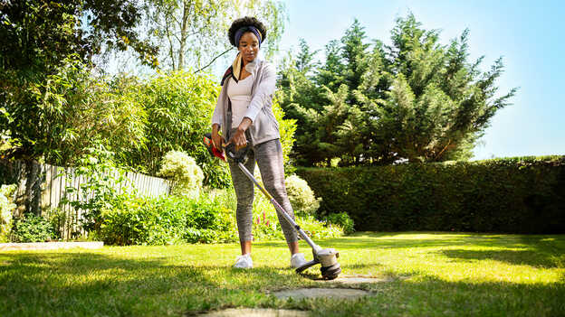 Femme utilisant le coupe-bordure à batterie Honda sur la pelouse d'un jardin.