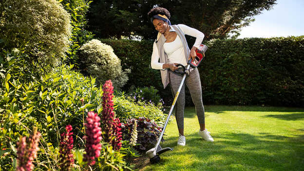 Femme utilisant le coupe-bordure sans fil Honda sur la pelouse d'un jardin pour montrer que les plantes sont protégées.