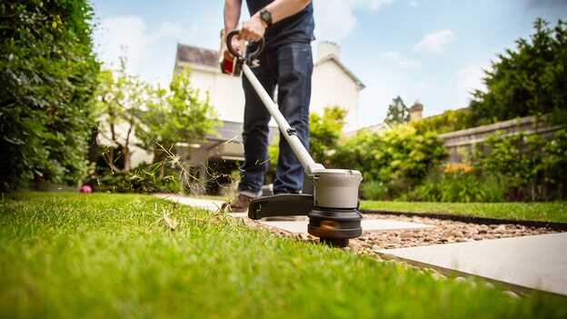 Homme utilisant le coupe-bordure à batterie Honda sur la pelouse d‘un jardin.