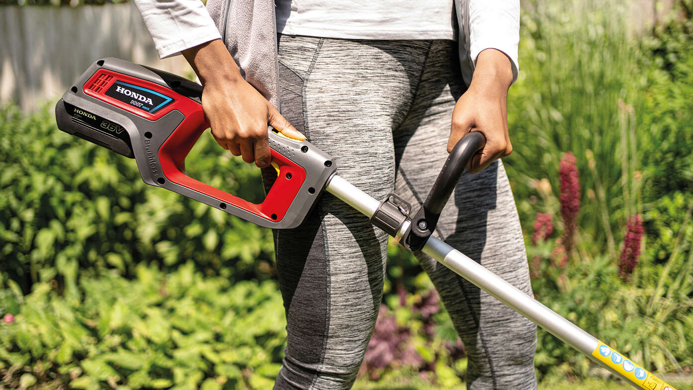 Gros plan sur une femme utilisant un coupe-bordure à batterie Honda dans un jardin.