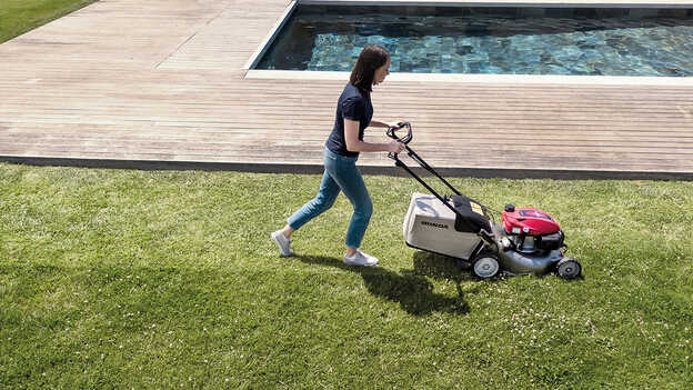 Vue latérale de la tondeuse à gazon Honda IZY avec un bac de ramassage de grande capacité dans un jardin