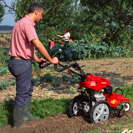 Motobineuse équipée d'outils rotatifs utilisée par un démonstrateur dans un jardin.