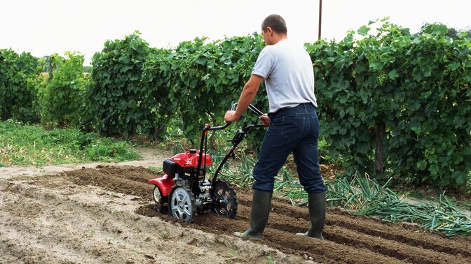 Motobineuse équipée d'outils rotatifs utilisée par un démonstrateur dans un jardin.