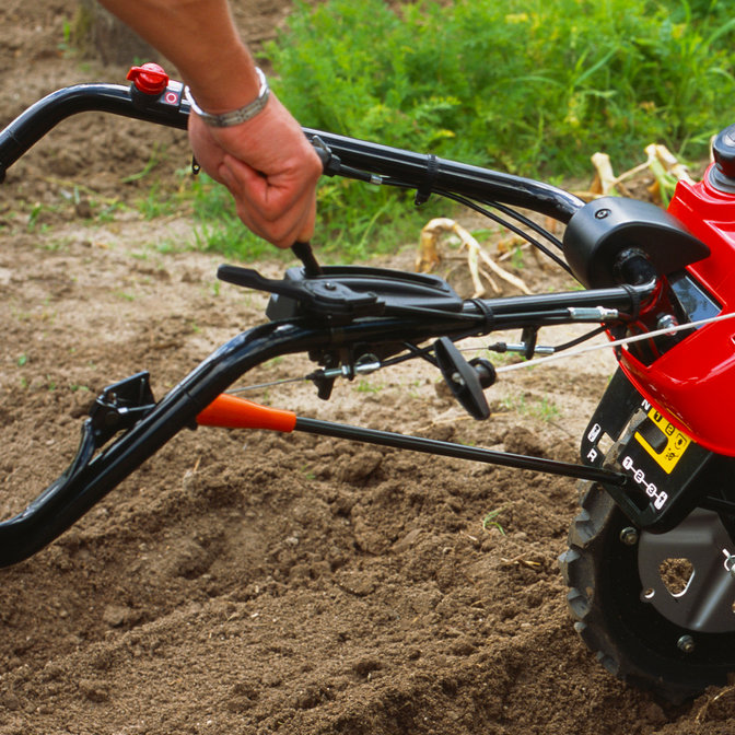 Gros plan du levier de vitesses d'une motobineuse équipée d'outils rotatifs, dans un jardin.