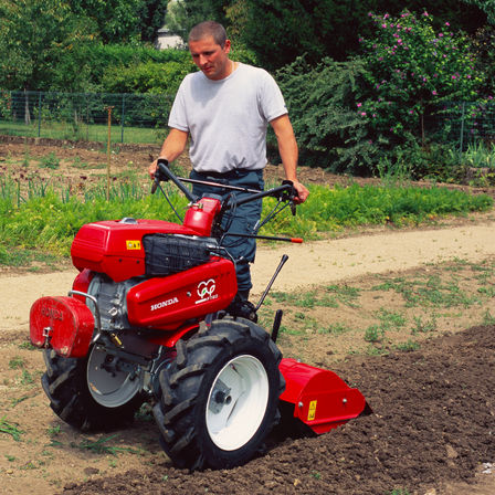 Motoculteur transformable utilisé par un démonstrateur dans un jardin.