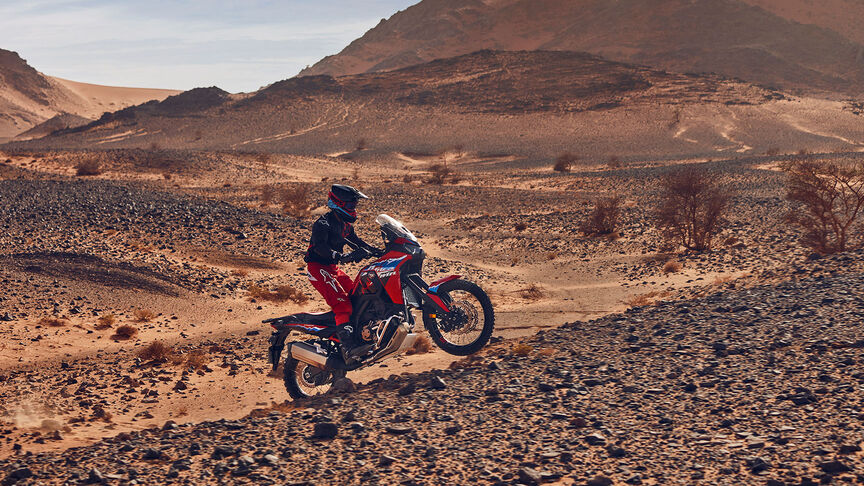 Mannequin roulant à bord d’une moto CRF1100L Africa Twin dans un environnement désertique.