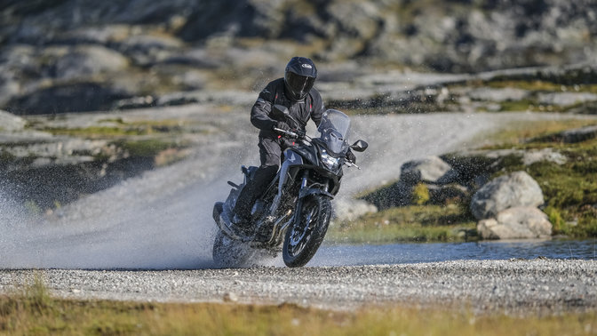 Honda CB500X pilotée en traversant un cours d'eau.