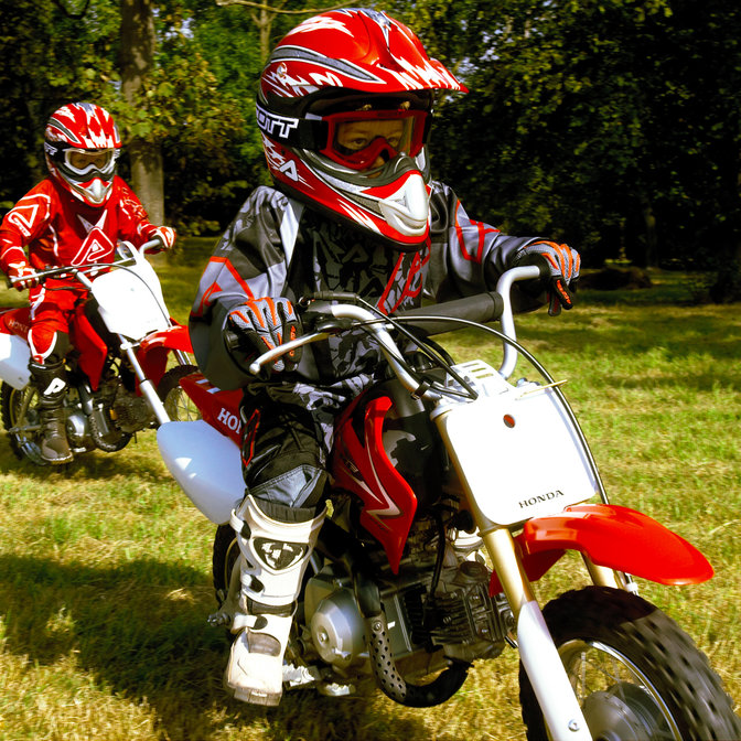 Vue de trois quarts latérale de 2 motos CRF50F avec conducteurs, pendant une course sur herbe. Vue de droite.