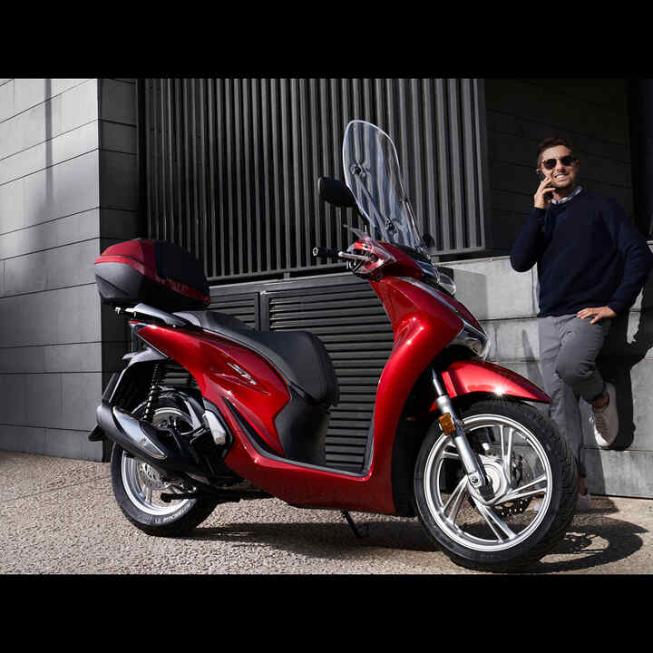 Homme au téléphone se tenant à côté d'un scooter Honda.