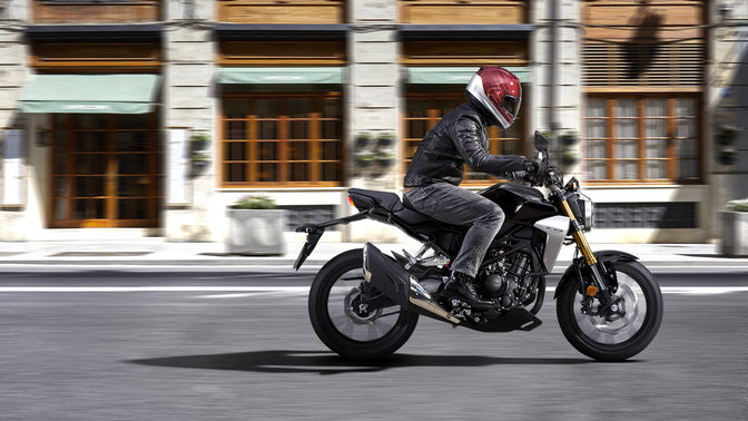 Vue latérale de la Honda CB300R Neo Sports Café conduite sur une route.