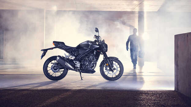 Vue de profil de la Honda CB300R à l’arrêt dans un garage avec un homme marchant en direction de la moto.