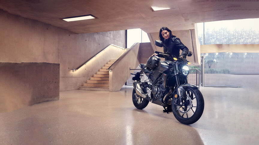 Vue de trois quarts avant de la Honda CB300R contemplée par une femme dans un studio.