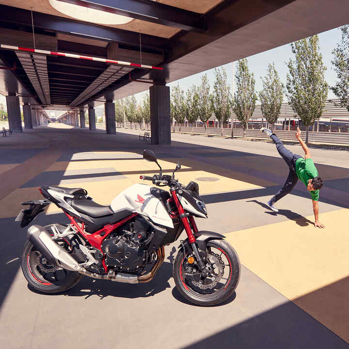 moto roadster streefighter Honda CB750 Hornet - permis A2 sous le pont avec un homme qui fait du breakdance.