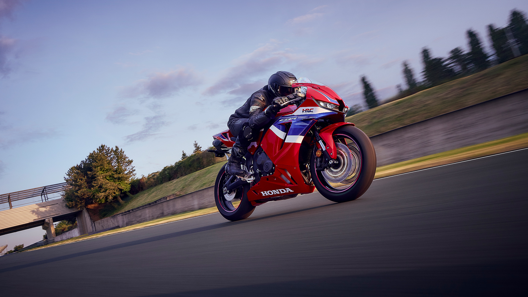 CBR600RR sur circuit avec motard dans un virage en plein coucher de soleil.